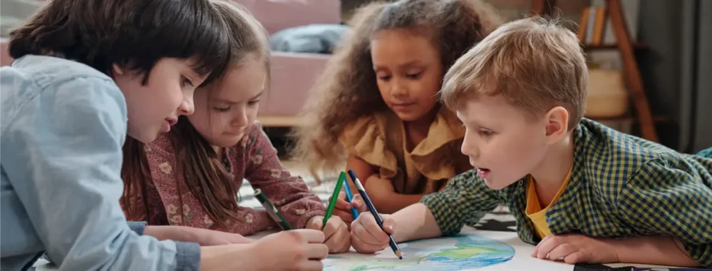 Diverse children drawing planet Earth with coloured pencils on the floor