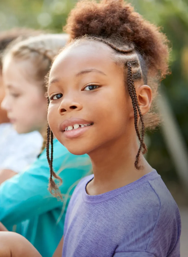 Young girl with creative braided hairstyle smiles at the camera.