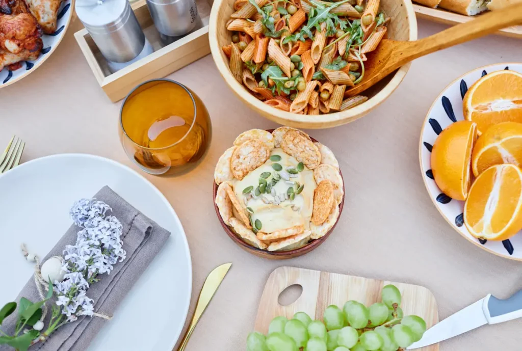 Platter of appetizers with pasta salad, brie, oranges, grapes and chicken.