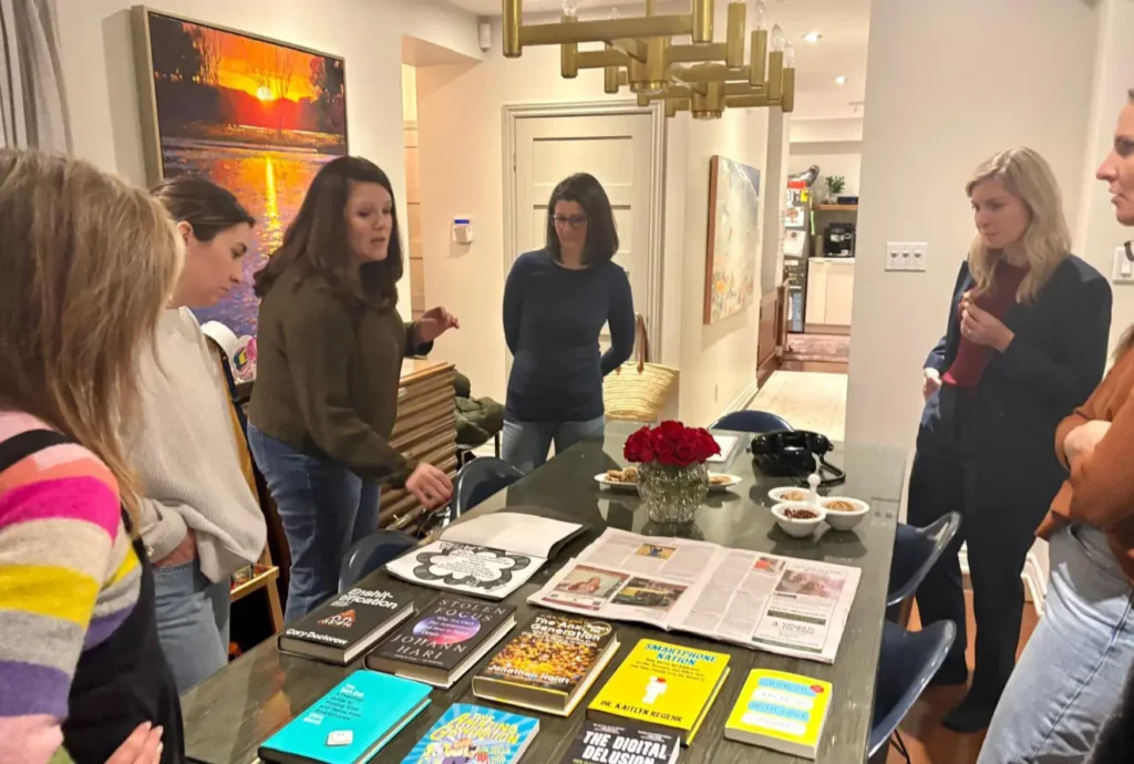 Group of women gathered around a table with books and newspapers for discussion.