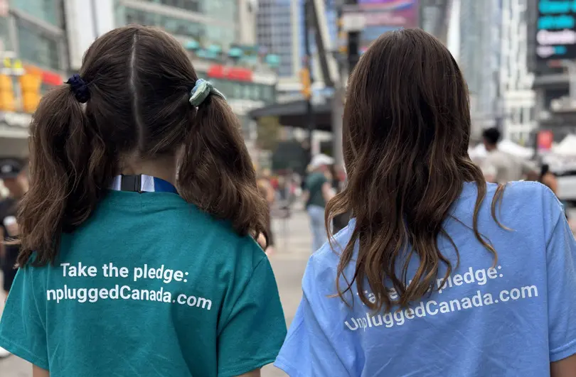 Two girls with pigtails and wavy hair wear t-shirts with "Take the pledge: UnpluggedCanada.com