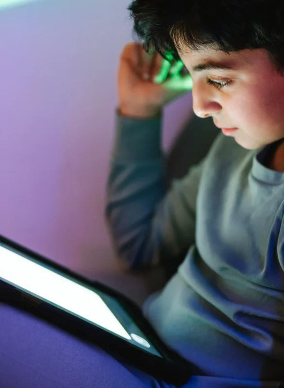 Young boy engrossed in a tablet screen, bathed in purple and green light.