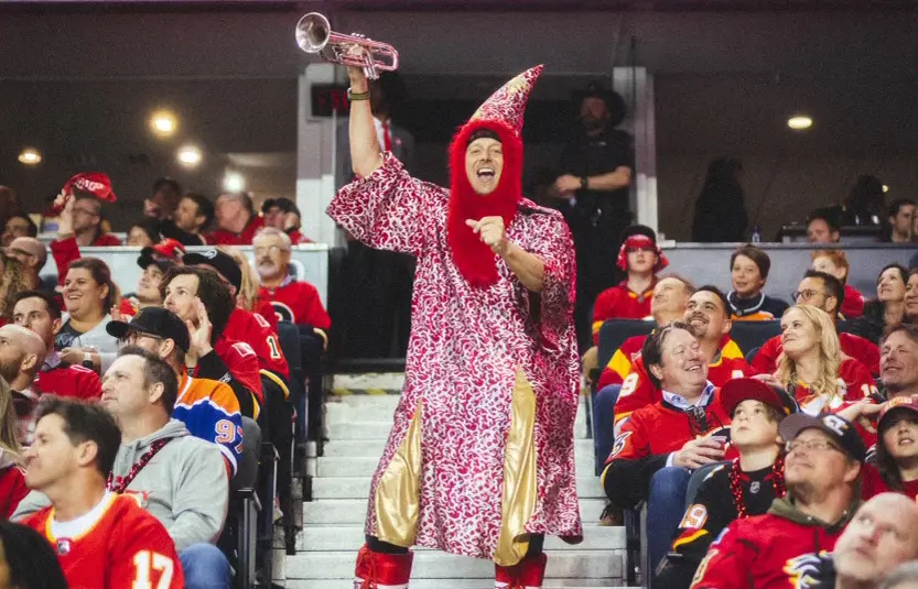 Fan in wizard costume plays trumpet in stadium cheering crowd.