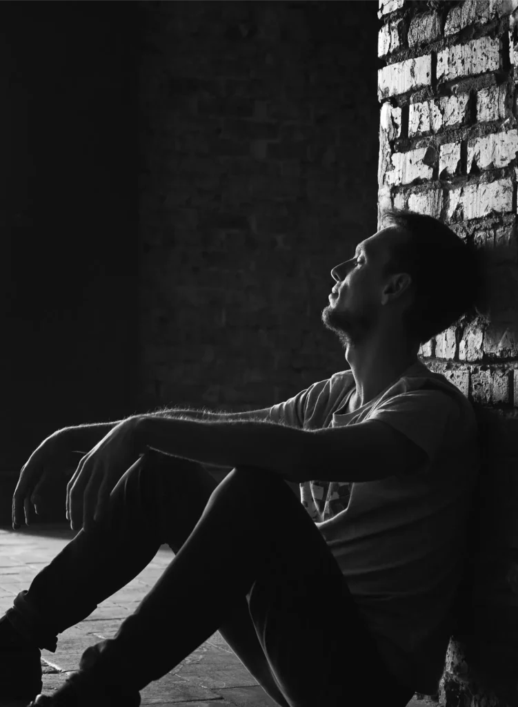 Man sitting against brick wall, head tilted back, looking up.