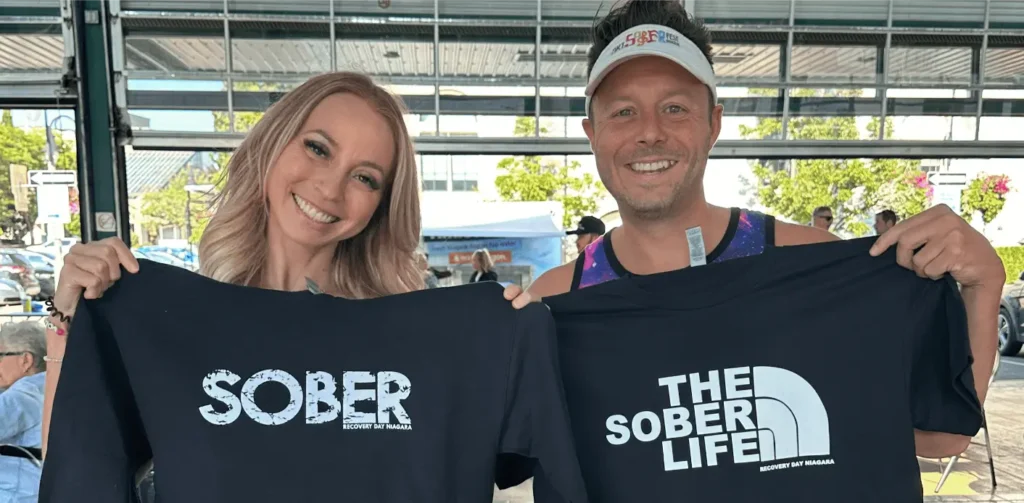 Two people hold up black t-shirts promoting sober living and Recovery Day Niagara.
