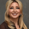 Blonde woman in brown shirt smiling with sparkling earrings