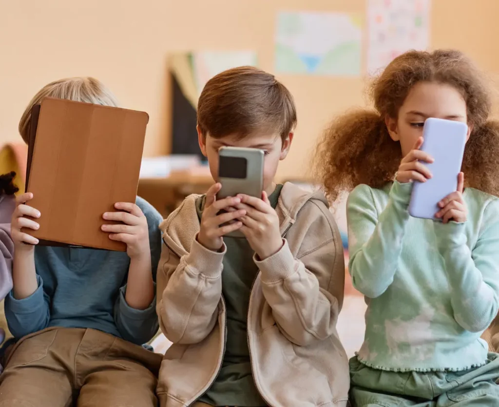 Children engrossed in phones, tablets, and a book, learning or playing.