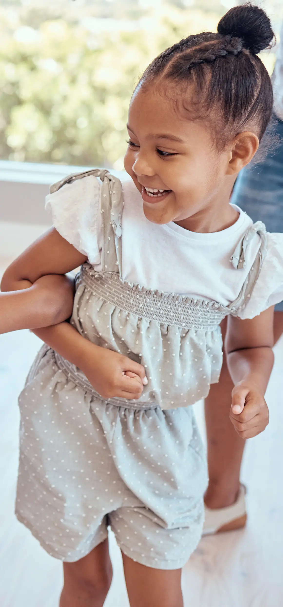 Smiling young girl with braided hair in a polka dot romper plays with hands clasped