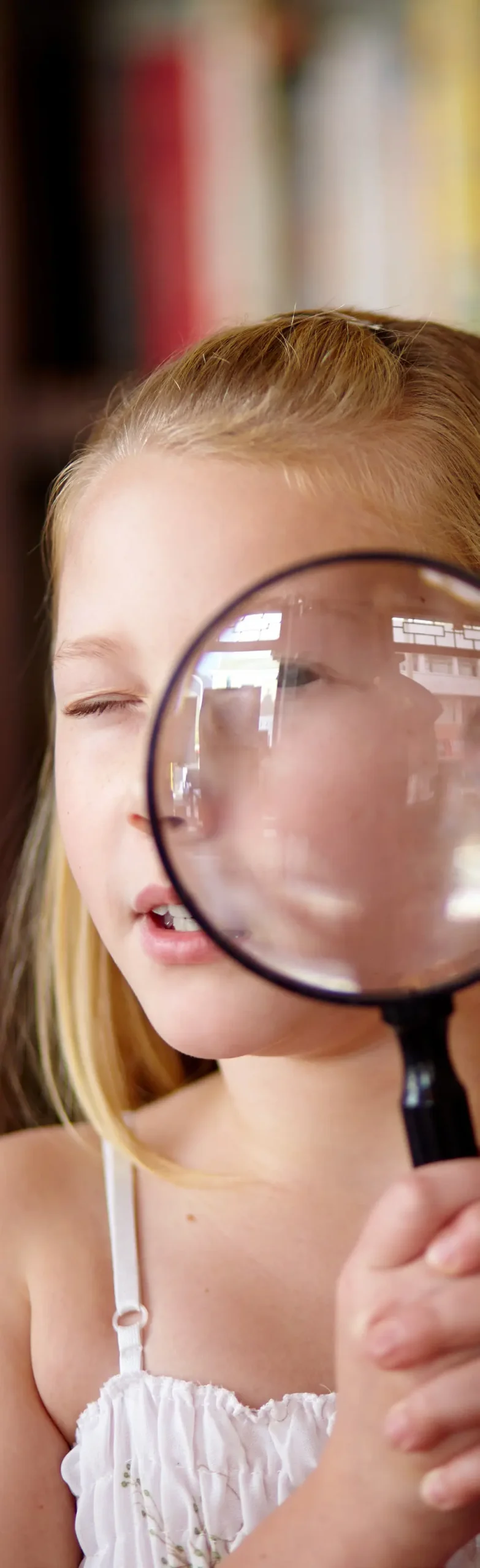 Young girl peers through a magnifying glass, exploring the world around her.