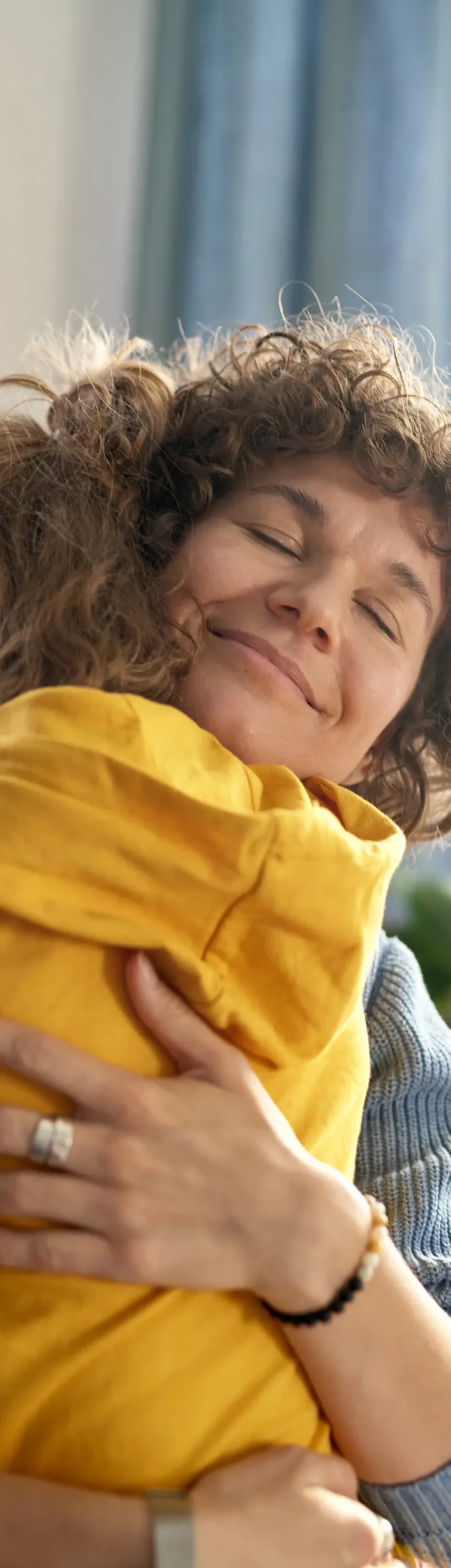 Woman with curly hair closes eyes, smiling and hugging a yellow cushion.