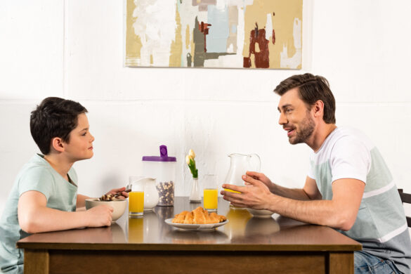 Father and son talking at breakfast table with cereal and juice.