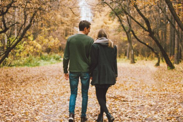 Couple walking hand in hand on a leaf covered path in an autumn forest