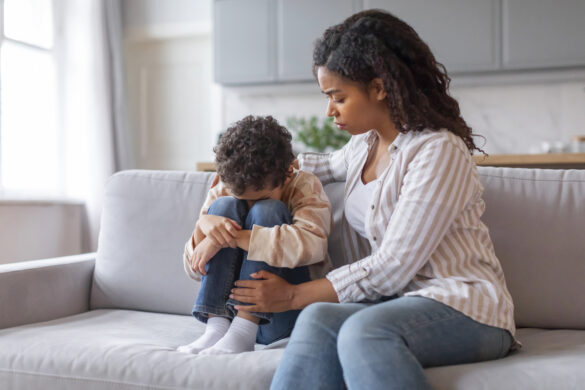 Mother comforts upset child sitting on a sofa.