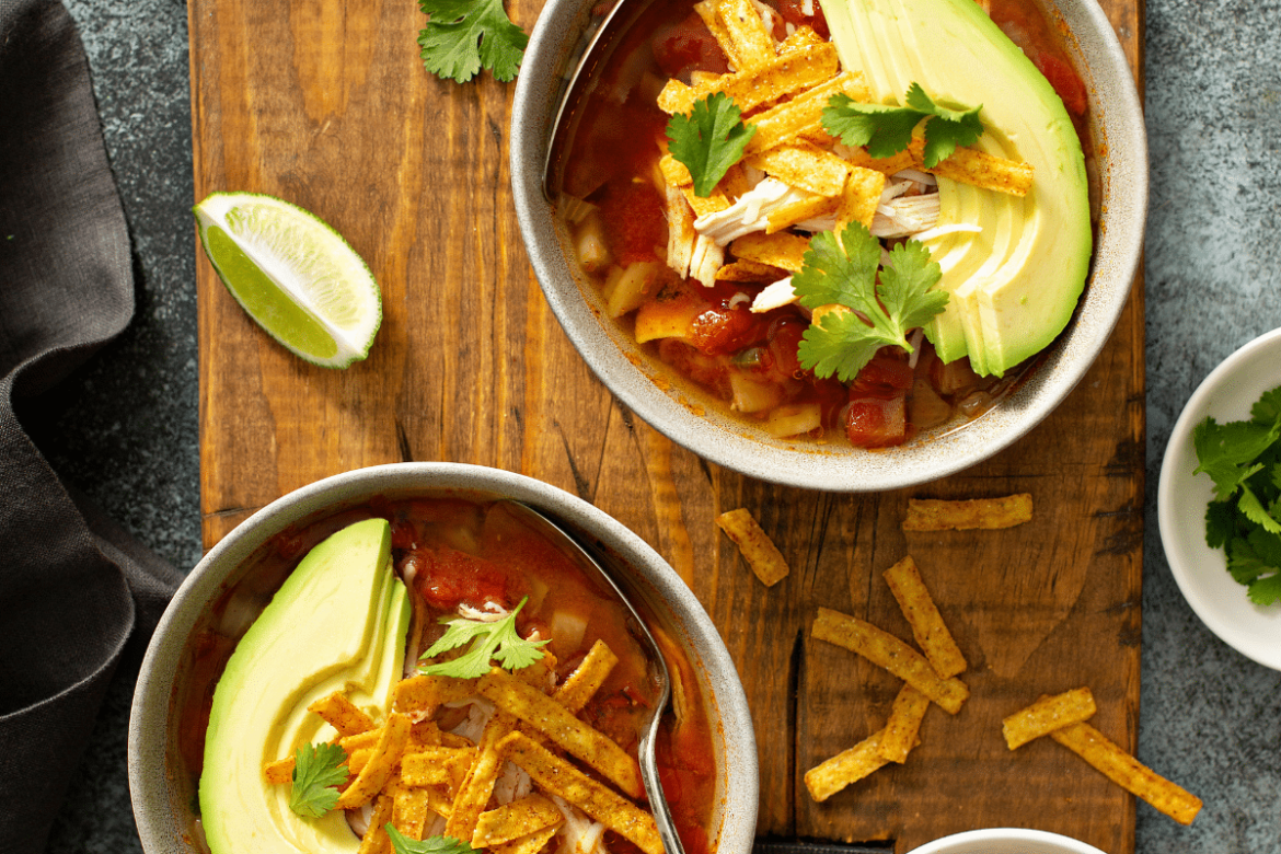 Two bowls of chicken tortilla soup with avocado, cilantro and lime wedges